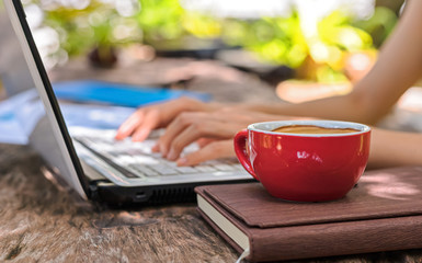 Cup of coffee on the book near business women working on laptop.