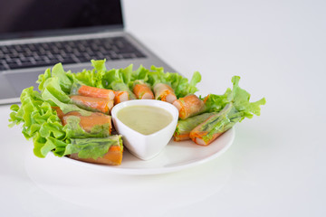 Crab stick and vegetable salad in noodle tube and sauce on white dish near laptop on table. Space for text. Health foods concept