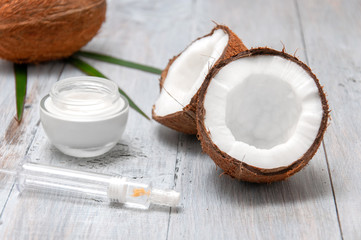 Coconut bisected, cream and syringe with hyaluronic acid on a gray wooden table. Personal care. Spa treatments. Cosmetology. Natural and organic cosmetics.