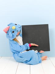pretty blonde girl with cozy blue unicorn costume and blackboard is posing in the studio in front of blue wall and is happy