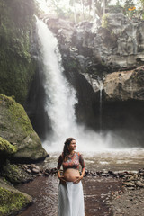 Young authentic pregnant woman near amazing cascade waterfall. Maternity time. Harmony with nature, travel in pregnancy. Tegenungan, Ubud, Indonesia