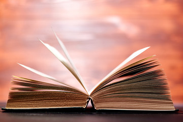 An opened thick book backlit by light on a brown background.