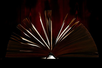 An opened thick book backlit by light on a brown background.