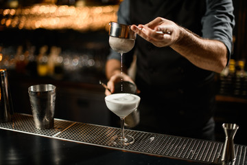 Bartender mixes the alcohol drink and uses a sieve