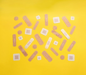 Different types of sticking plasters on yellow background, flat lay