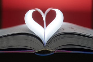 A heart from book pages shines in on a brown background.