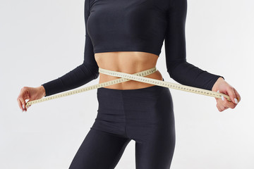Close up view of sportive woman with measuring tape in the studio against white background