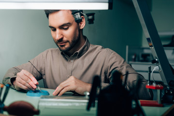 Selective focus of watchmaker working with watch parts in tool tray at table