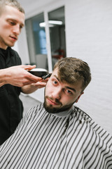 Man with a beard visits a barber shop, a barber repeats creating a hairstyle with a clipper in his...