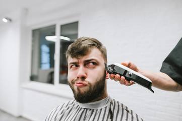 Portrait of a funny bearded man haircut in a men's hairdresser and with a funny face looks away at...