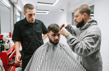 Barbershop. Professional barber teaches a student to cut a model in a men's shop. Two men trimming a bearded model in a barbershop. Workshop on men's haircuts.