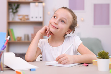 Fototapeta premium Cute little girl is doing homework in the interior of the room.