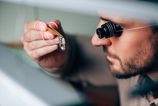 Side view of handsome watchmaker in eyeglass loupe looking at wristwatch part
