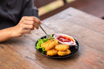 Chicken Nuggets impaled on a fork  and Dip sauce. A women eat Nuggets.