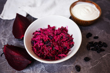 Obraz na płótnie Canvas A light simple salad of beets and raisins with sour cream on a dark gray marble background. Around - the ingredients. The concept of simple homemade food, healthy eating.