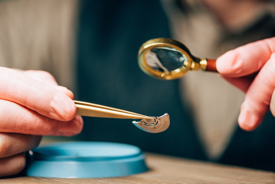 Cropped view of clockmaker working with magnifying glass and watch detail by tool tray on table