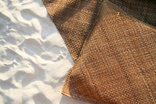 Directly Above View Of Straw Blanket And Cushion On White Sand At Beach