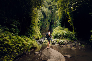 Young beautiful traveler with backpack standing on the little mountain hill with forest on the...