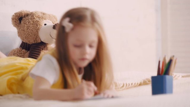 Selective focus of teddy bear by kid drawing on bed