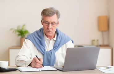Mature Man At Laptop Working Taking Notes Sitting In Office