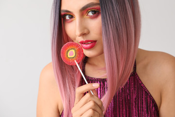 Beautiful young woman with lollipop on light background