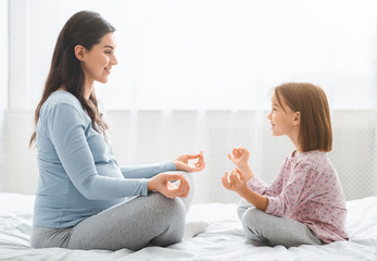 Expecting mother and little daughter doing yoga together