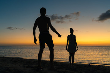 Silhouettes of a young couple on the beach on a summer sunset background  
