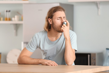 Sick man with inhaler in kitchen at home