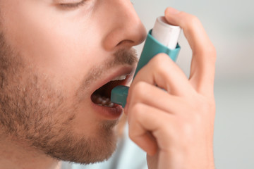 Sick man with inhaler at home, closeup