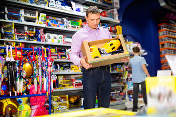 Portrait of positive adult man buying toy cement mixer machine in modern toy store