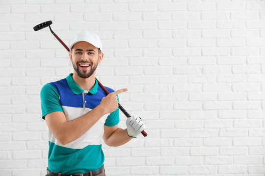 Handsome male golfer pointing at something on white brick background