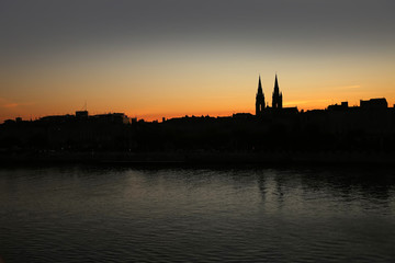 Fototapeta premium Silhouette of the skyline of the city of Bordeaux, at sunset with church steeples & the river Garonne in the foreground, France.