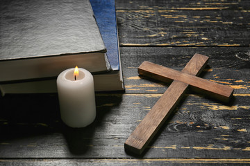 Christian cross, candle and Bible on dark wooden background