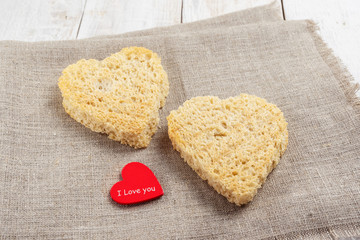 Bread cut in the shape of hearts and a red heart on a linen napkin on a white wooden background.