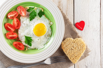 Breakfast on plate, fried eggs with tomato and bread in the shape of a heart. Romantic food.