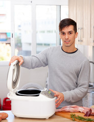 Smiling man cooking with electric multicooker