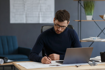 Architect working in office with blueprints.Engineer inspect architectural plan, sketching a construction project.Portrait of handsome bearded man sitting at workplace. Business construction concept.
