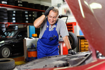 Puzzled male mechanic inspecting broken car and determining scope of work at auto service