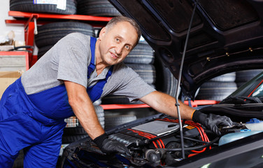 Fototapeta na wymiar Portrait of confident male mechanician posing near car at auto service