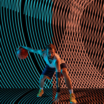 Creative sport on dark neon lighted line background. Basketball player training in action and motion on colorful waves. Concept of hobby, healthy lifestyle, youth, action, movement, modern style.