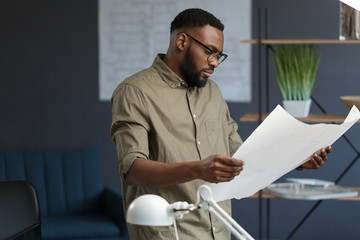 Afro-American architect working in office with blueprints.Engineer inspect architectural plan,...