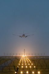 in front of a runway, a airplane at start at foggy weather, yellow bright guiding light, behind a barbed wire fence, dusk