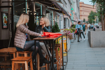 Two young women friends met in a city street cafe and have fun chatting.