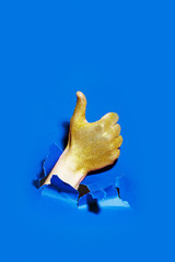 Hand with golden glitter break through the paper with the thumb up.