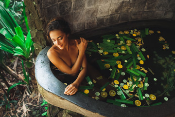 Beautiful young woman enjoying in outdoor spa. Luxury stone bath tub with jungle view. Natural...