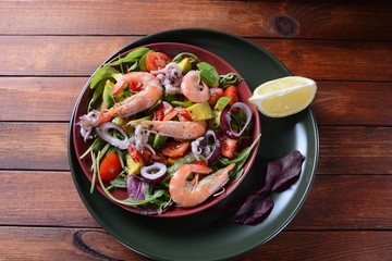 Sea food salad with shrimps, avocado, cherry tomatoes, red hot chilly pepper, red onion, arugula, beet leaves,rukola.balsamic sauce in a plate on a wood background Healthy sea food concept