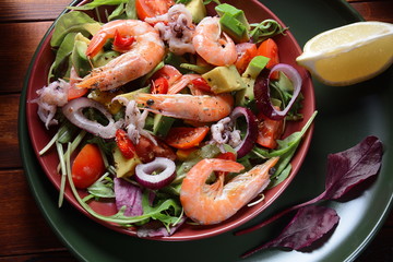 Sea food salad with shrimps, avocado, cherry tomatoes, red hot chilly pepper, red onion, arugula, beet leaves,rukola.balsamic sauce in a plate on a wood background Healthy sea food concept