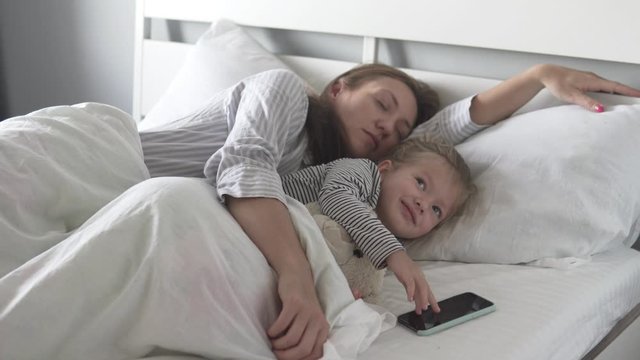 A woman wakes up from an alarm bell next to her sweet daughter in the morning in the bed