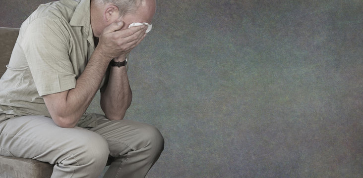 Mental Health Awareness Campaign for Men background banner - crying man with hands holding white tissue against eyes on a rustic neutral grey background with copy space for message