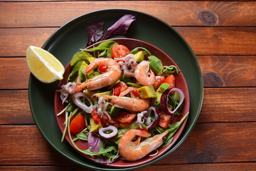 Sea food salad with shrimps, avocado, cherry tomatoes, red hot chilly pepper, red onion, arugula, beet leaves,rukola.balsamic sauce in a plate on a wood background Healthy sea food concept
